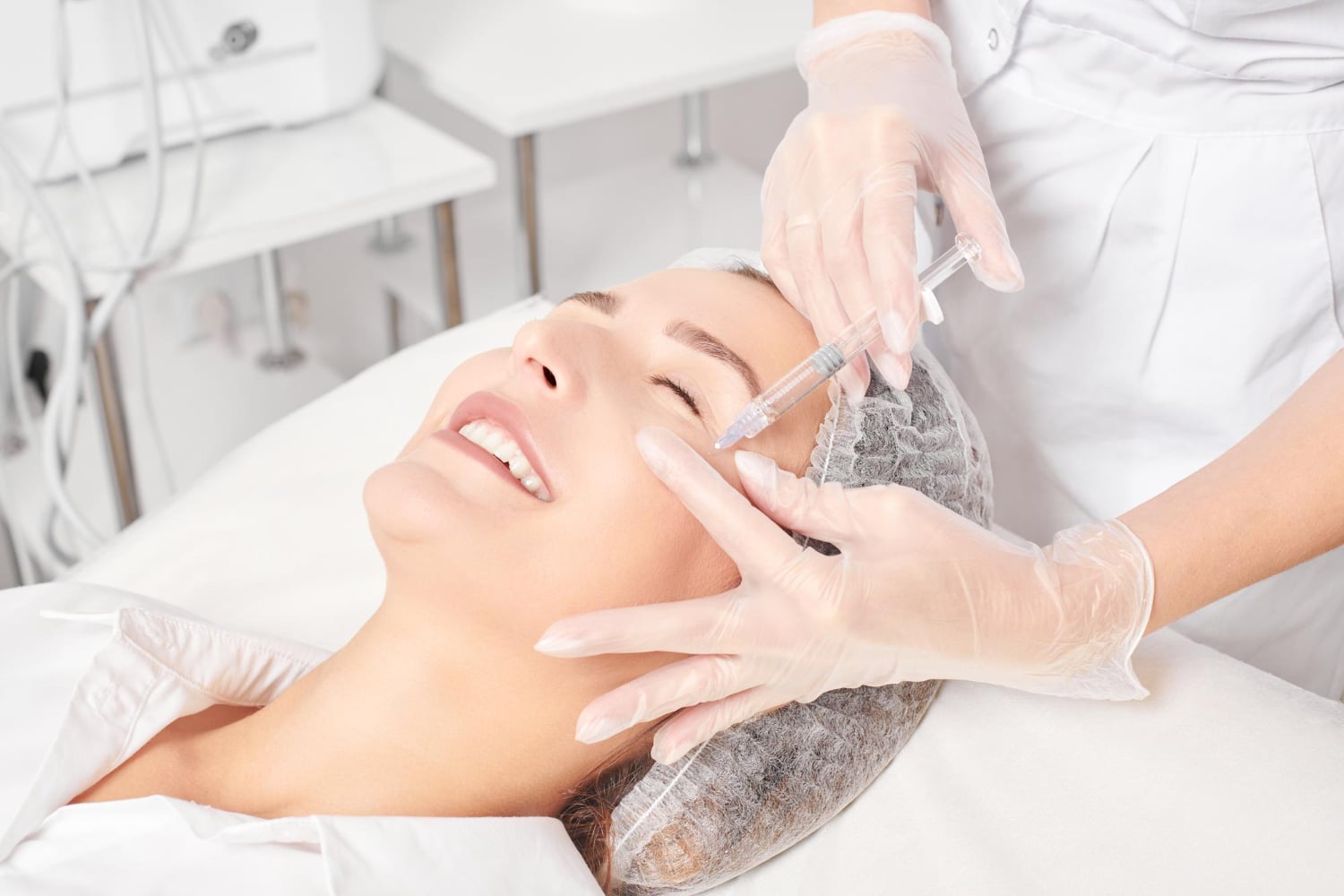 A person lying down receives an injection in the forehead from a medical professional wearing gloves in a clinical setting.