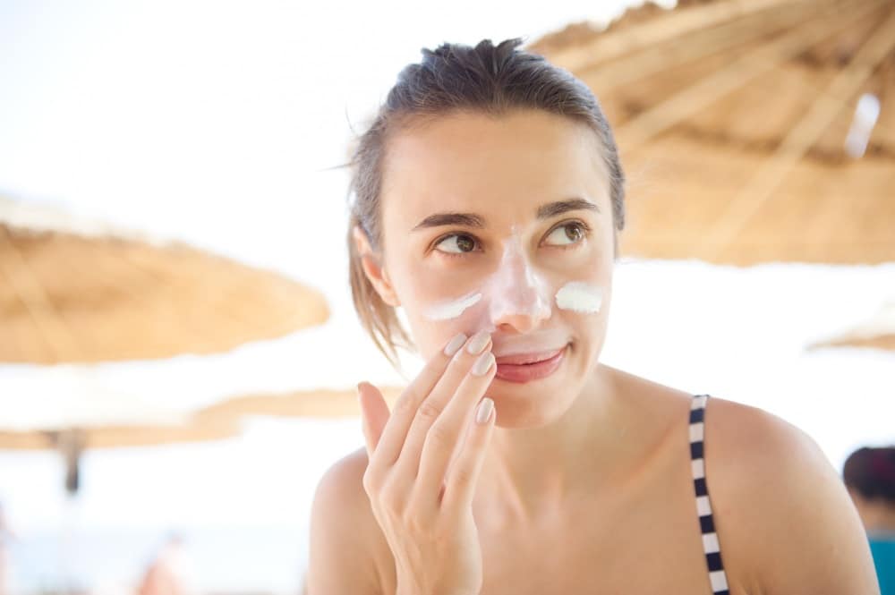 A woman applies suncream to her face whilst outdoors after IPL treatment for rosacea.
