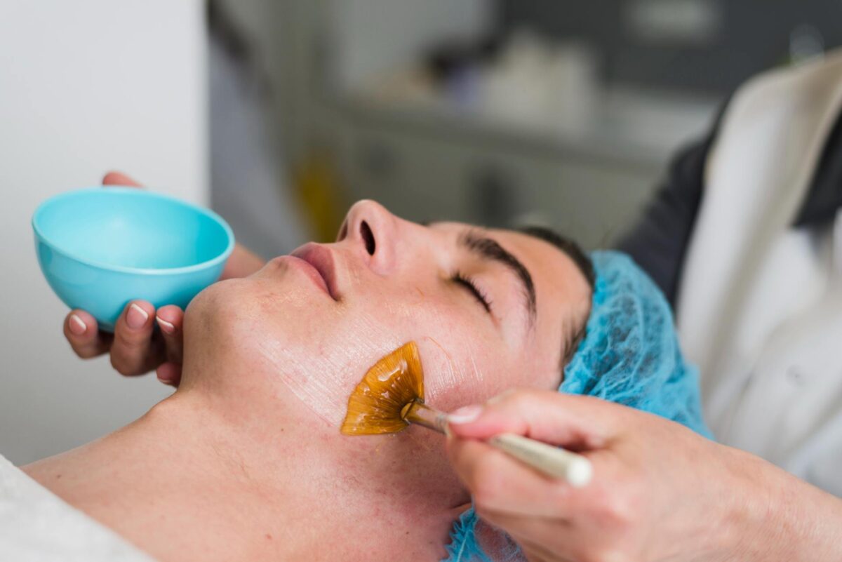 A person wearing a hairnet receives a chemical peel treatment as a practitioner applies a product to their face with a brush.