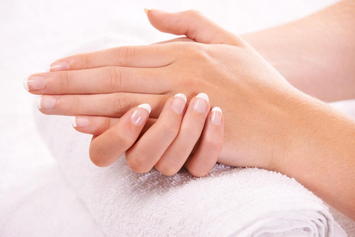 Close-up of hands with a French manicure resting on a rolled white towel, against a soft, neutral background—showcasing hands rejuvenation, the sign of ageing.