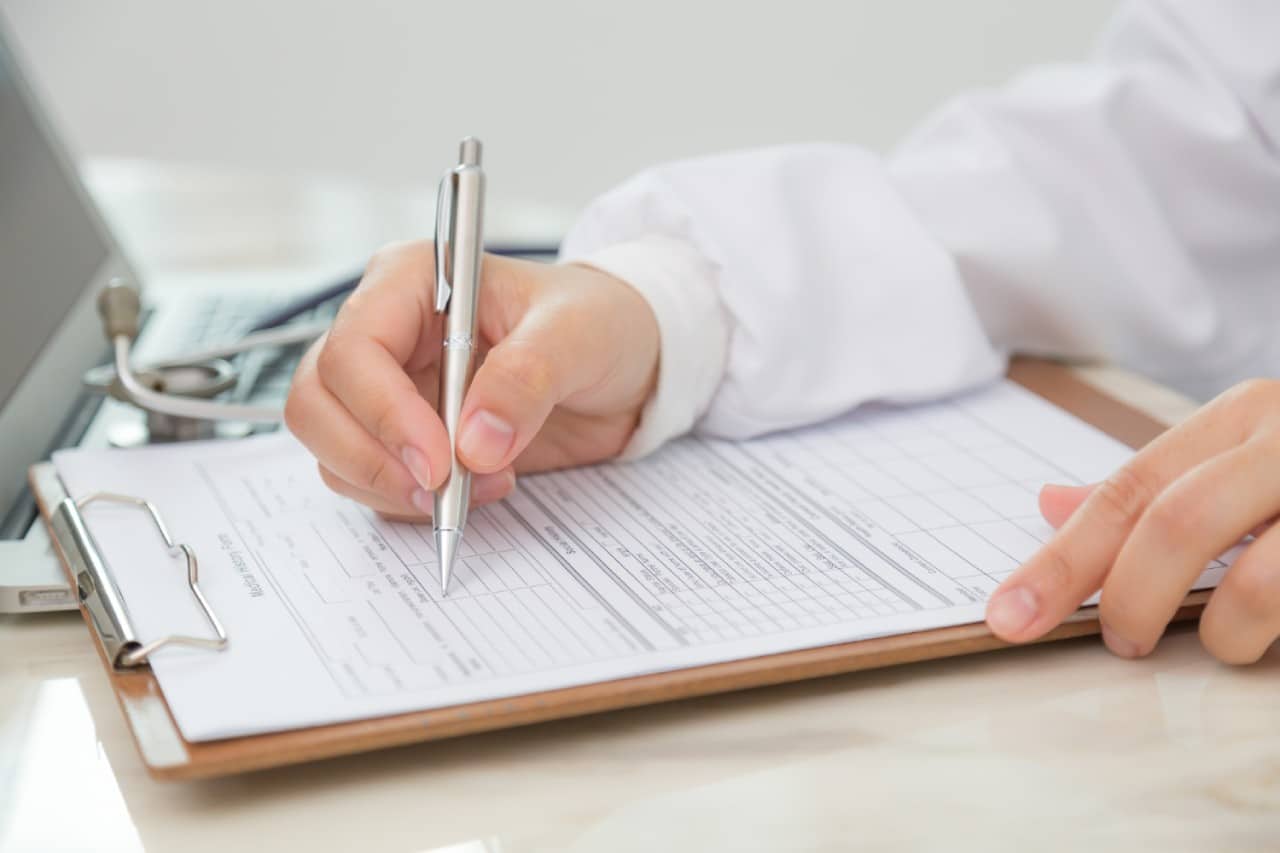 A person in a white lab coat filling out a list of questions to ask about injectable treatment at the consultation.