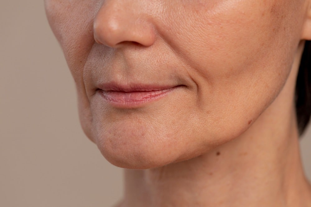 Close-up of the lower face of a middle-aged person with visible skin texture, wrinkles, and light laughter lines.