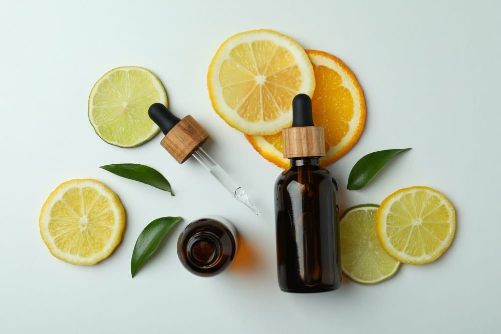 Two amber dropper bottles surrounded by lemon, lime, and orange slices, with green leaves on a white background.