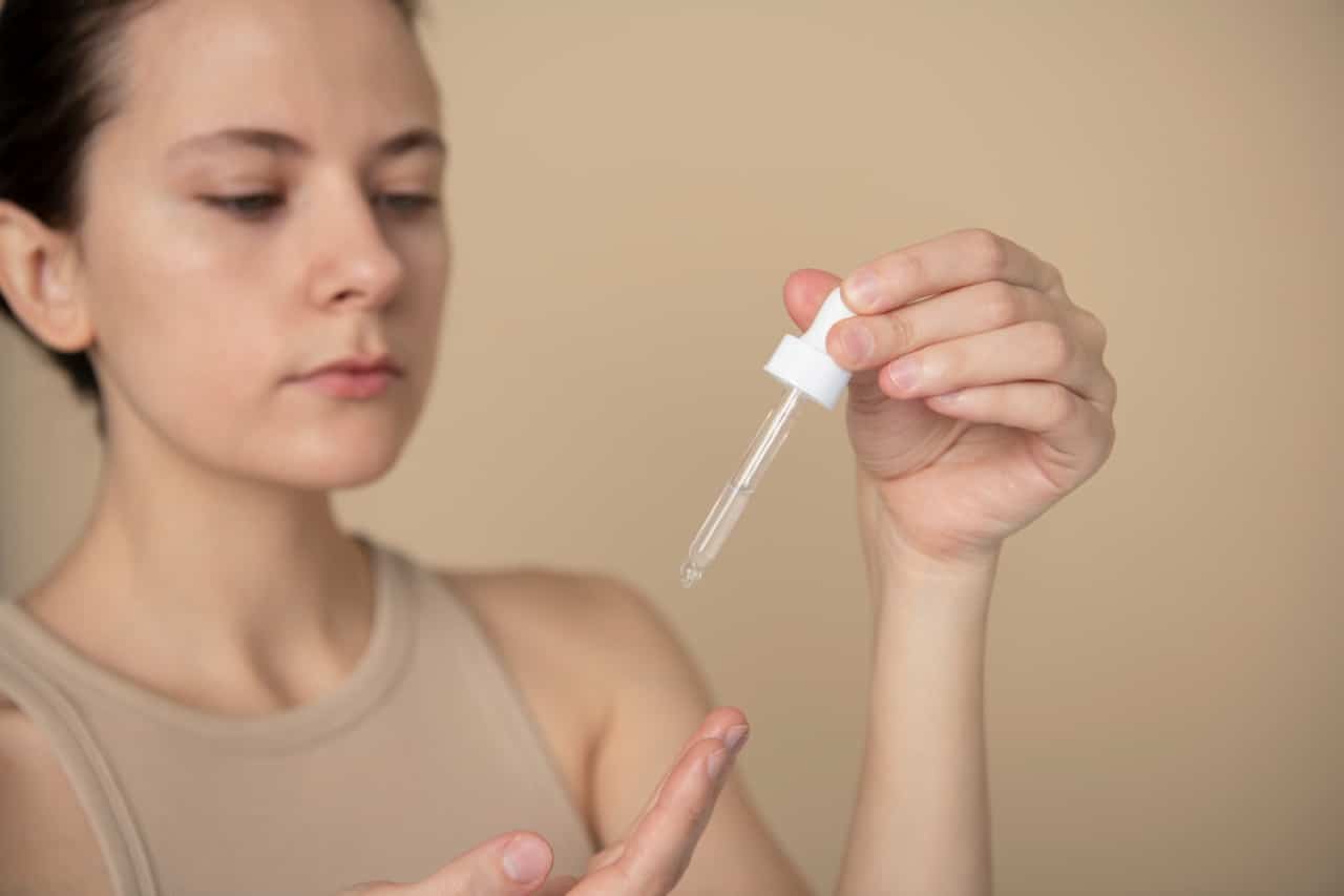 A person holding a glass pipette filled with a clear molecule skincare peptide for skin absoprtion.
