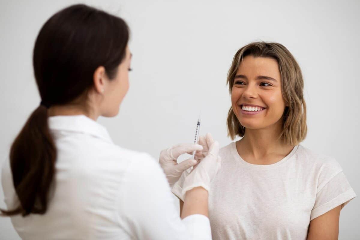 A medical professional in gloves holds a syringe in front of a smiling patient for an injectable treatment.