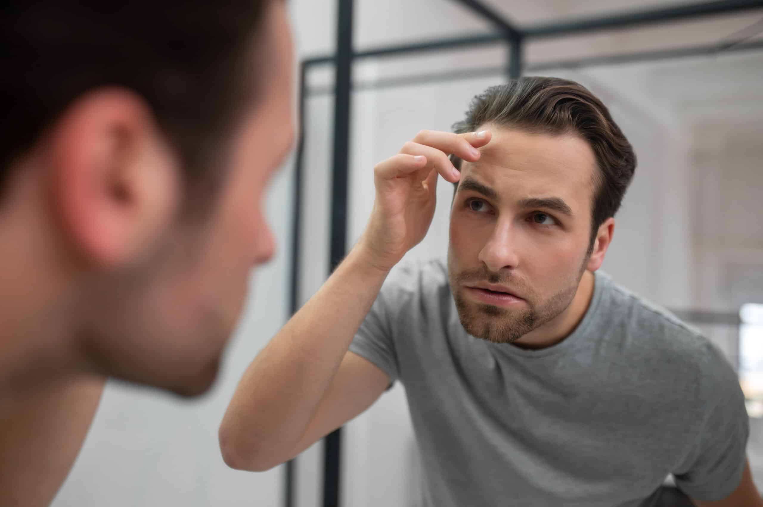 young man checking in mirror worrying about hair loss