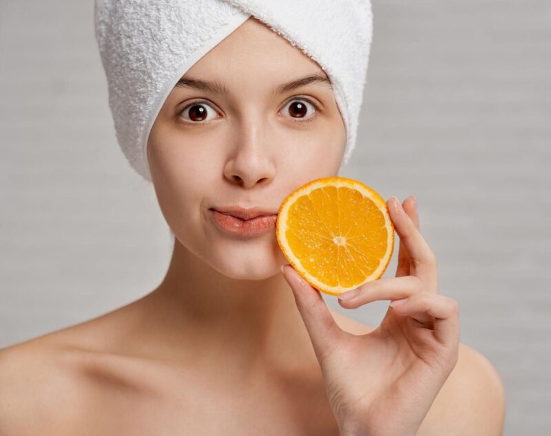 A young woman with beautiful, firm and natural skin holding an acidic orange