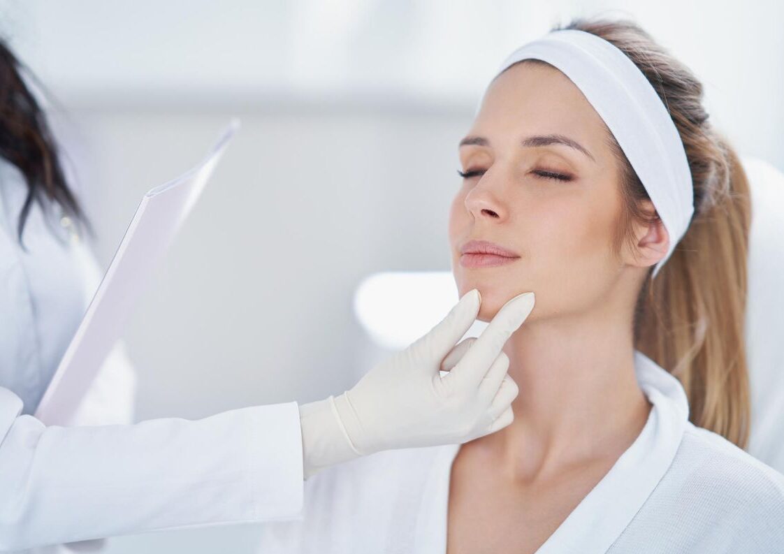 A cosmetic doctor examining a young woman's face before cosmetic treatment