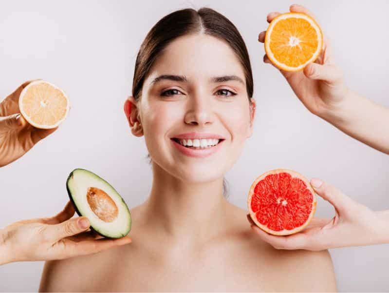 healthy beautiful radiant skin of woman without makeup. portrait of girl smiling against wall of fruits.