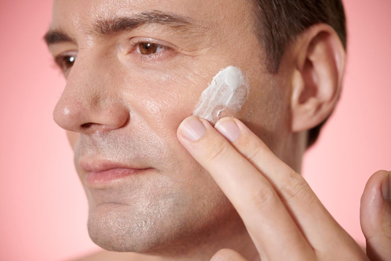 A man applying microbiome-friendly skincare cream to his cheek with his fingers.