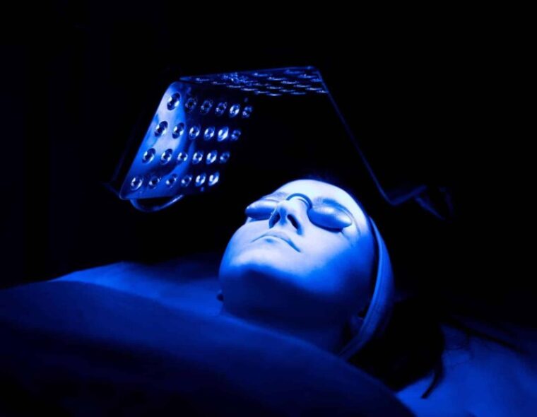 young woman having blue led light facial therapy treatment in beauty salon